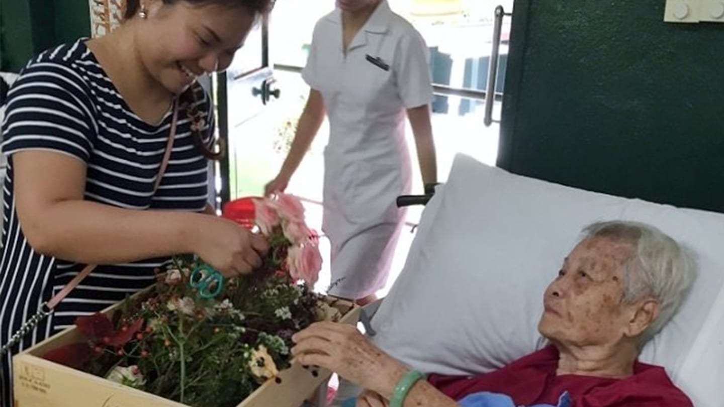 volunteer in striped shirt giving out bouquet to elderly patient in hospice