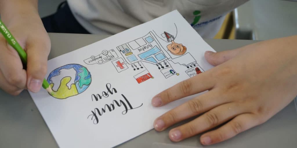 child colouring in a thank you card featuring a hospital and a globe