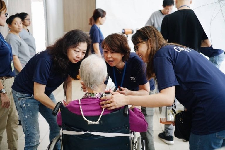 three female volunteers in blue shirts attending to a lady in a purple shirt sitting in a wheelchair