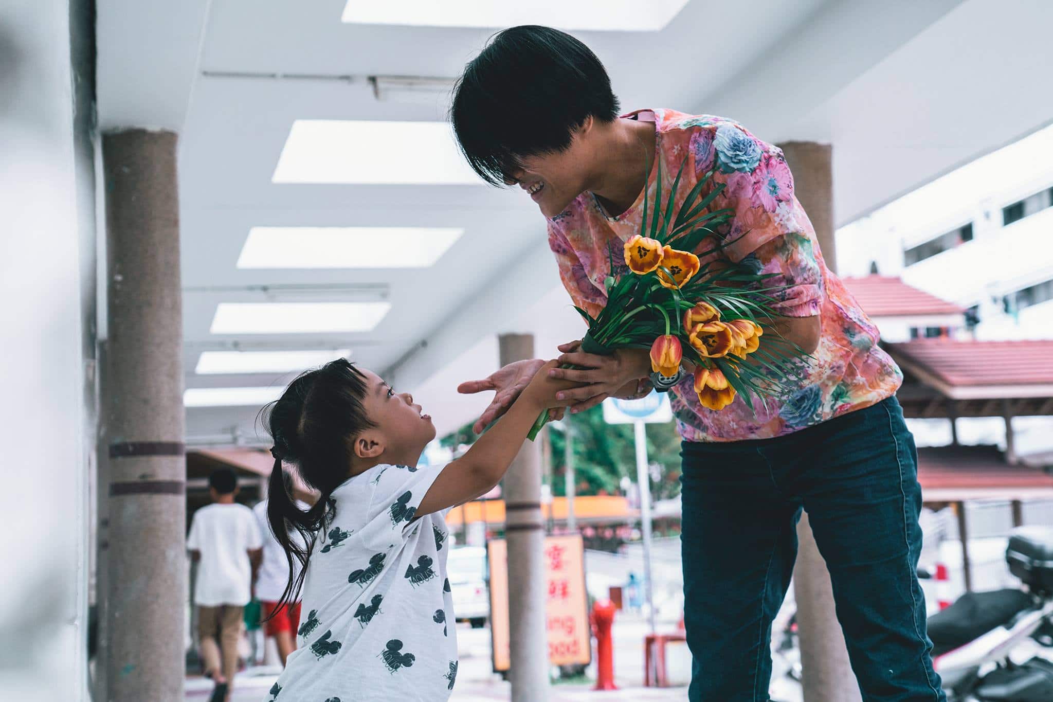man in flowery pink shirt bending down to hand girl a bouquet of yellow flowers