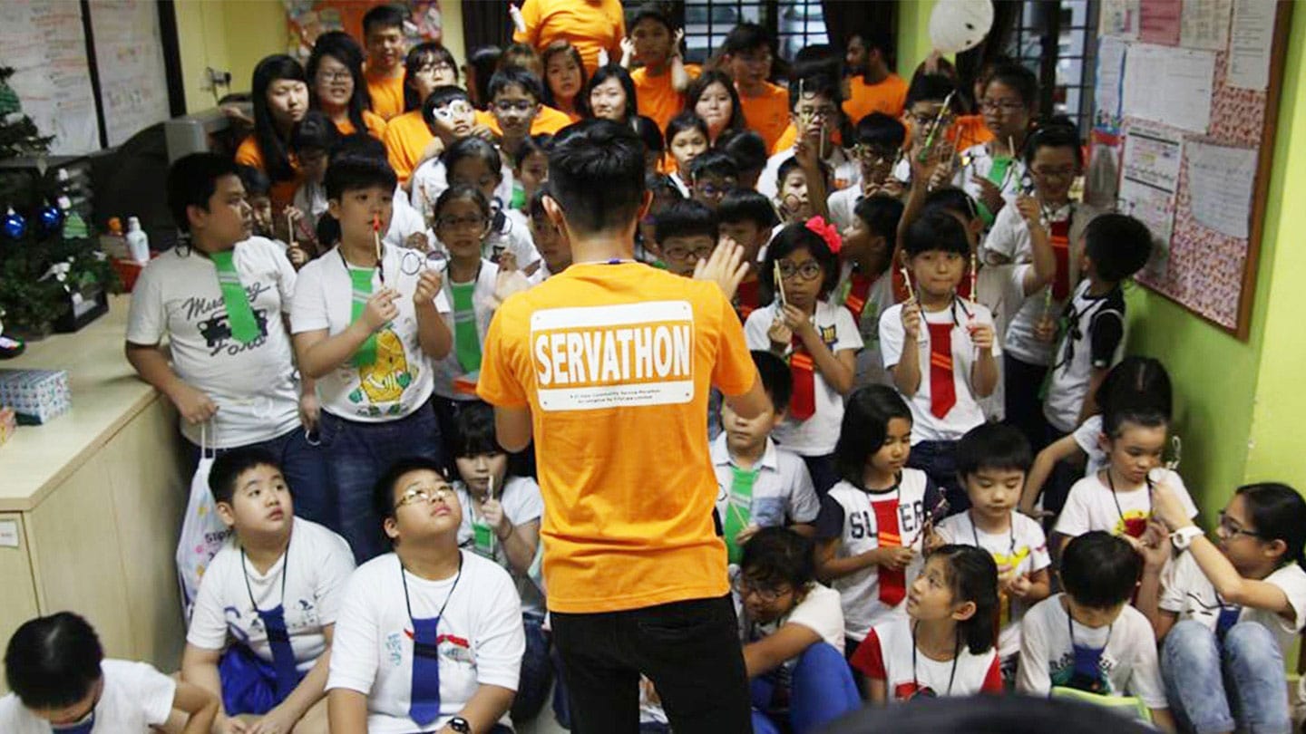 man in orange servathon shirt talking to kindergarteners in ties