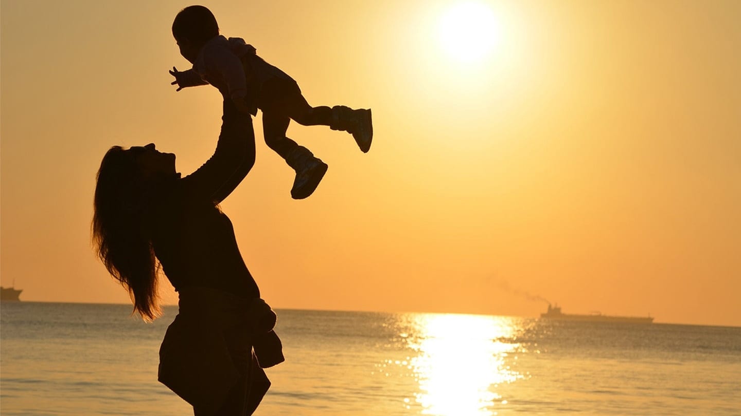mother lifting her child up as sun sets in the horizon