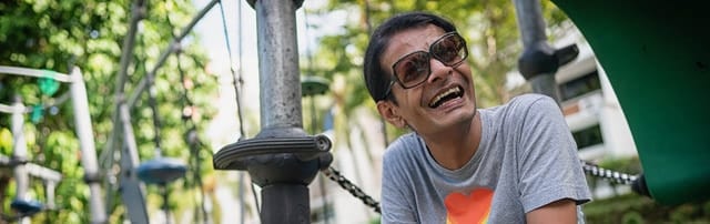 man in sunglasses and grey shirt laughing at exercise area