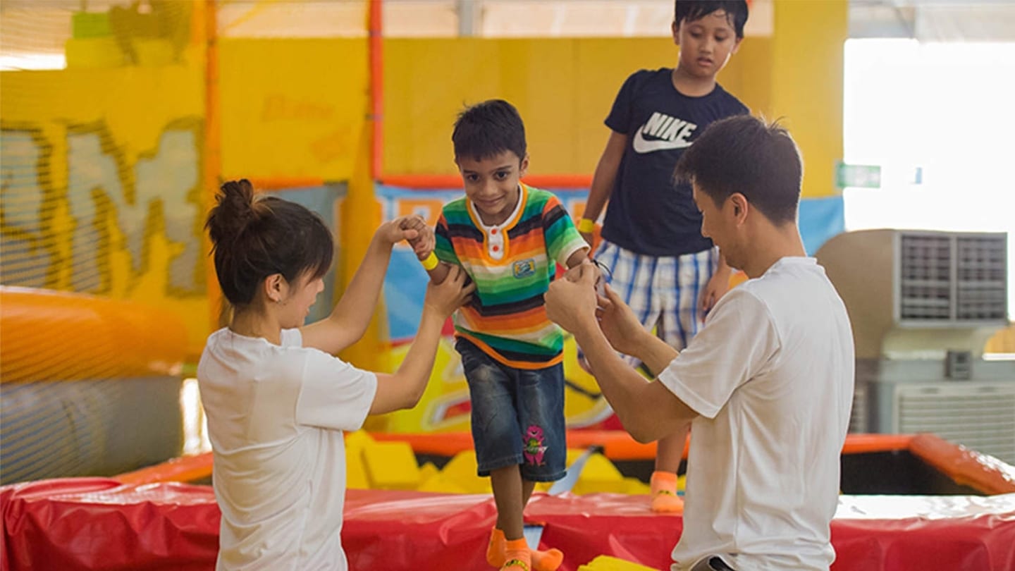 two volunteers helping indian boy down from inflatable castle