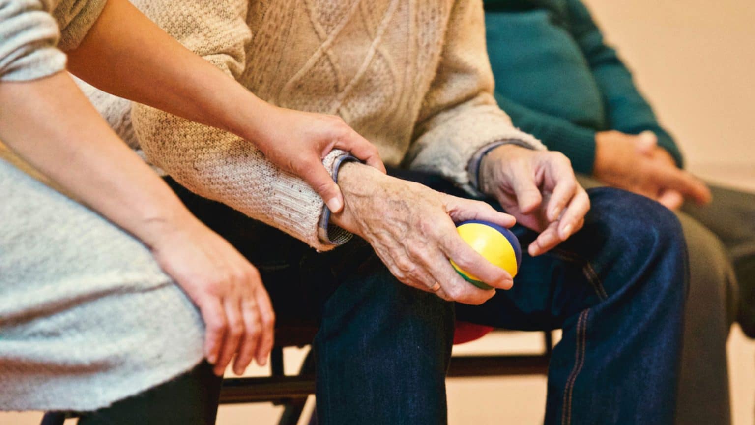 volunteer in grey shirt holding arm of elderly man holding a colourful ball