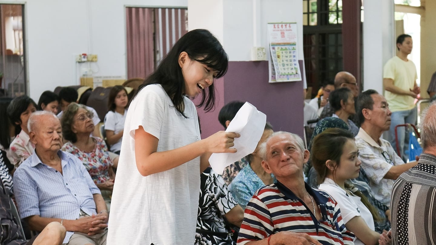 elderly participants and long-haired woman volunteer in a white shaired