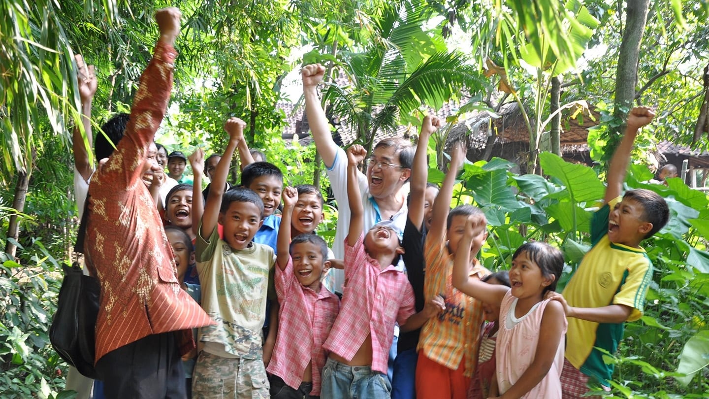 middle-aged man and native children pumping their fists in the air
