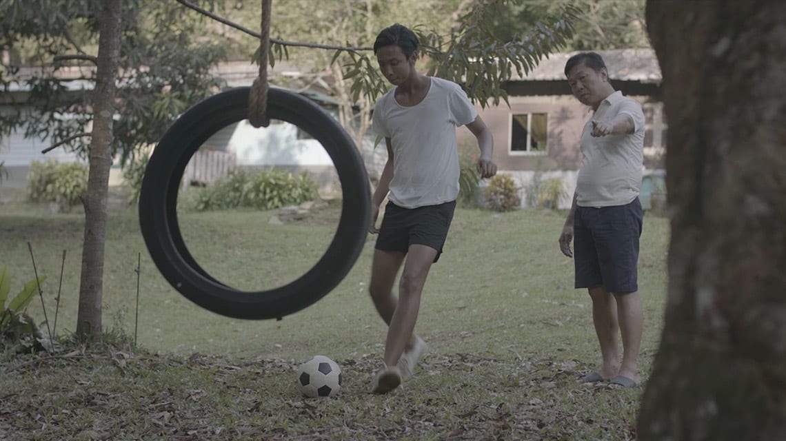 man coaching boy to play soccer in front of tire swing