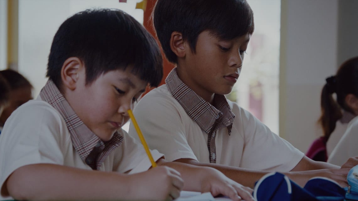 chinese and malay boy in brown uniforms taking notes in their notebook during a lesson