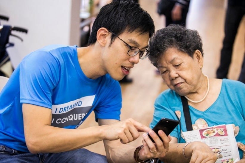 chinese man in blue shirt showing an elderly woman something on his phone