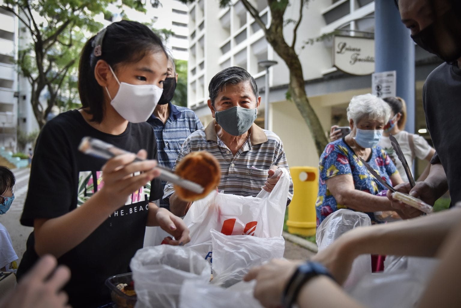 girl volunteer with black shirt handing bread to beneficiary using a pair of tongs