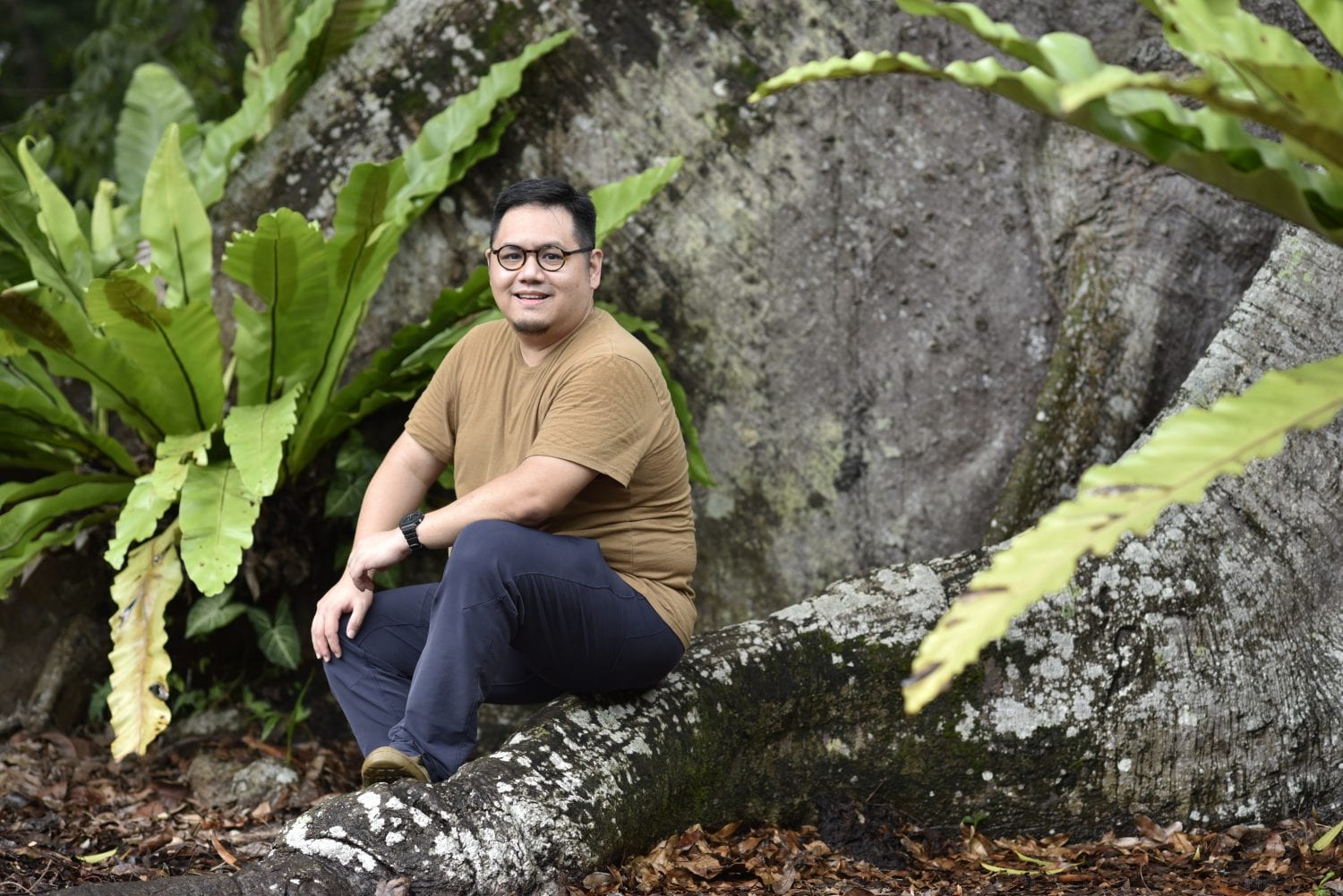 man in brown shirt sitting on a rock structure decorated with ferns