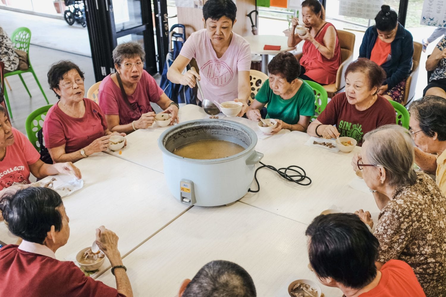 old women sitting around a table with a pot of soup in the middle